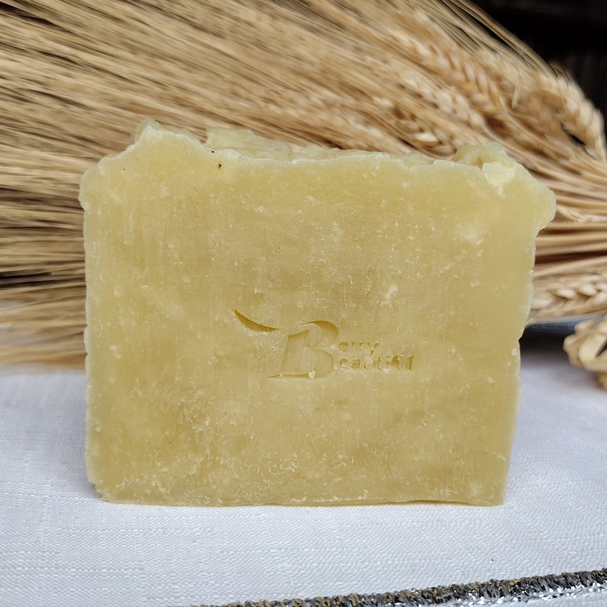 Bar of soap with a brand logo on a white surface with straw in the background