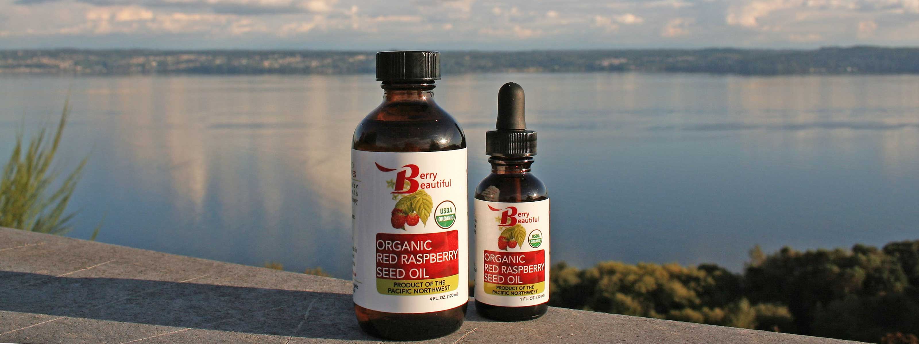 Photo of organic red raspberry seed oil bottles displayed on a deck railing. The scenic background features the Puget Sound, as seen from Vashon Island.