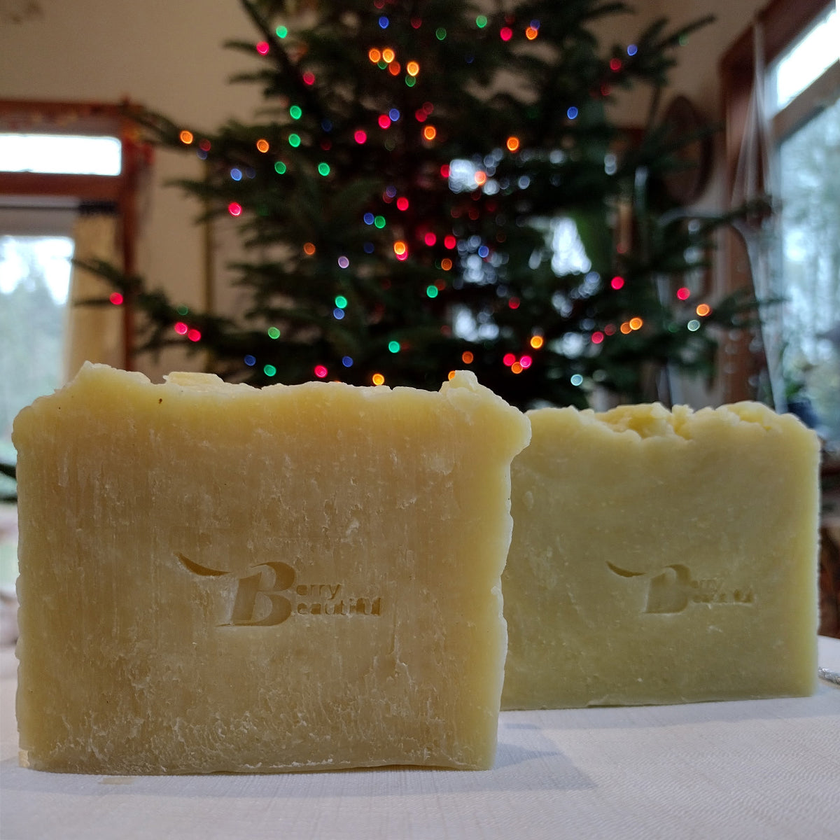 Two bars of soap with a brand logo in front of a decorated Christmas tree.