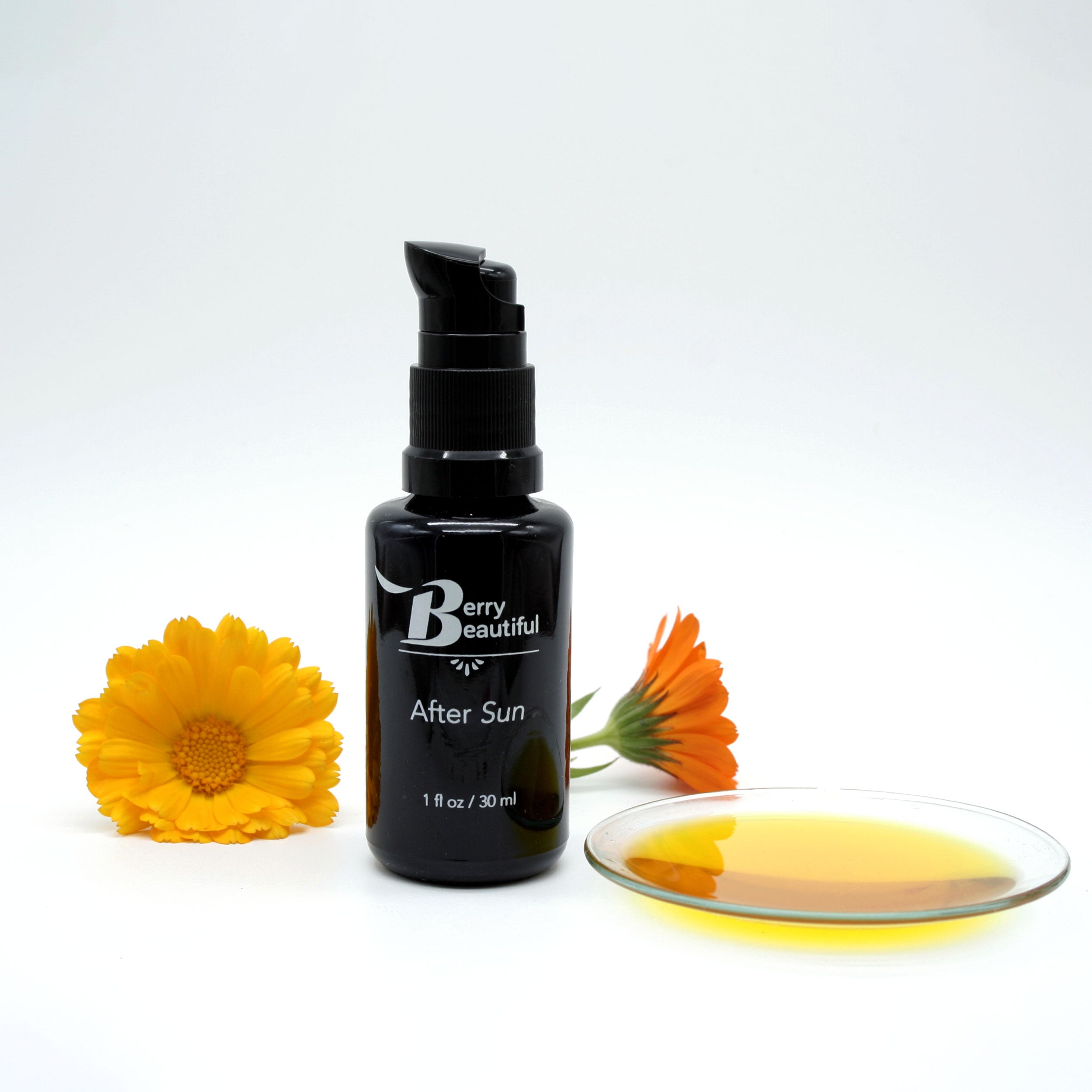 Berry Beautiful After Sun Serum in a Miron glass bottle, shown with freshly picked calendula flowers—one golden and one orange—and a clear dish displaying the golden color of the calendula and vanilla-infused raspberry seed oil.