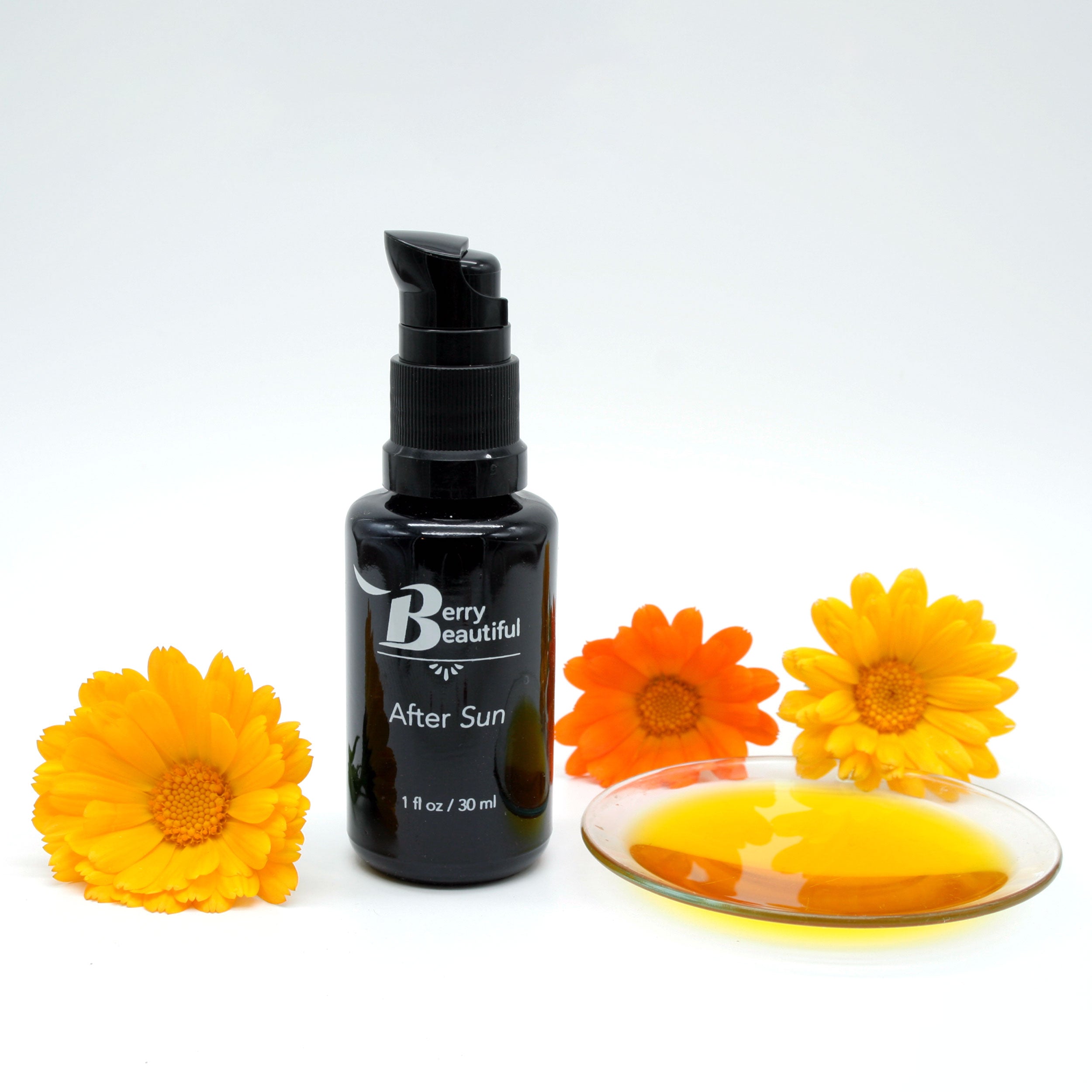 Berry Beautiful After Sun Serum in a Miron glass bottle, surrounded by three calendula flowers—one golden, one orange, and one yellow—and a clear dish showcasing the vibrant golden color of the infused raspberry seed oil.